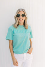 Model wearing a teal short sleeve tee shirt with Mama across the front in puff white letters.