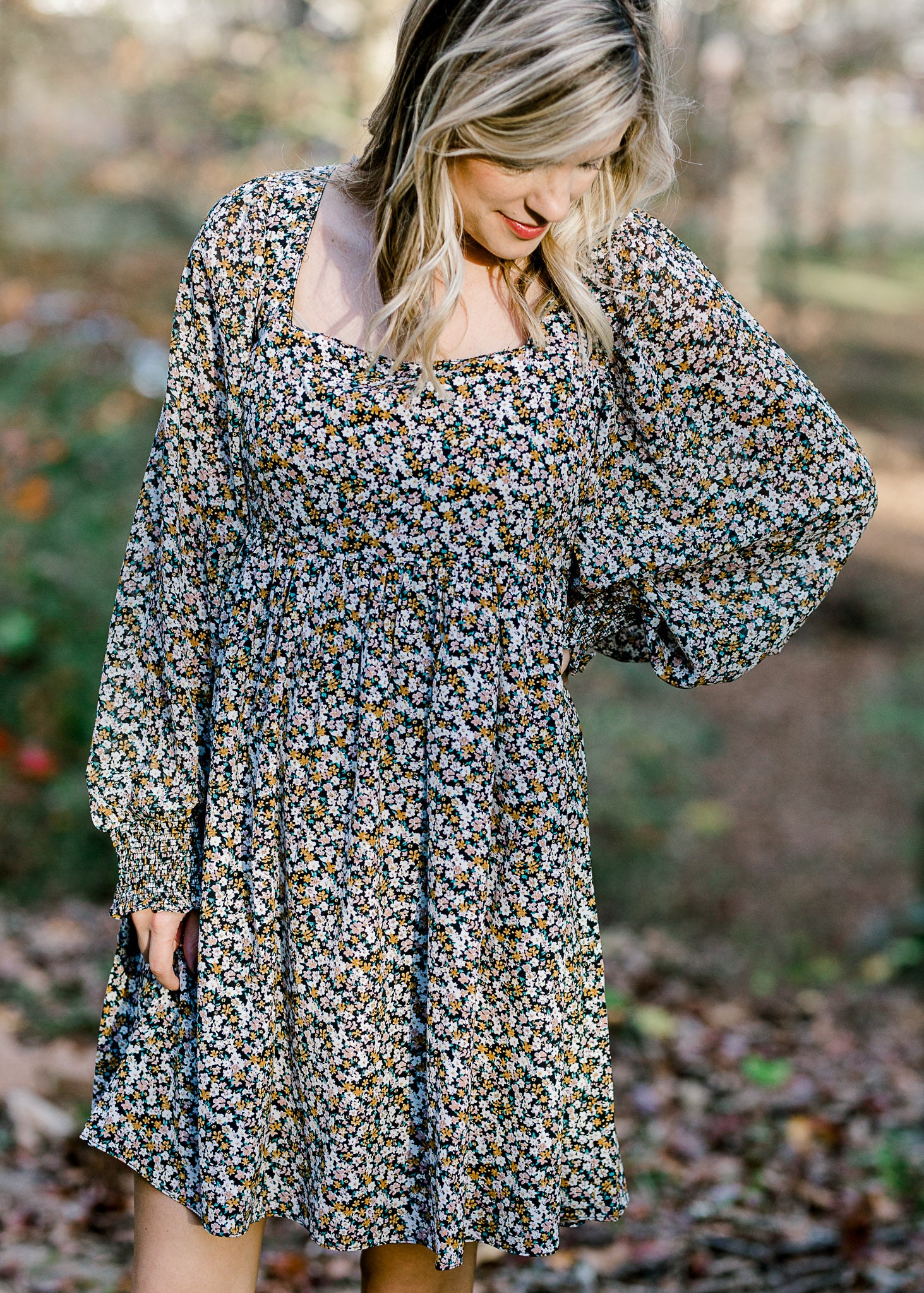 Blonde model wearing a black dress with camel and white floral pattern. 