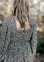 Back view of Blonde model wearing a black dress with camel and white floral pattern. 