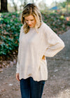 Blonde model wearing an off white sweater with exposed hem.