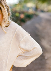 Close up view of exposed hem on off white sweater. 