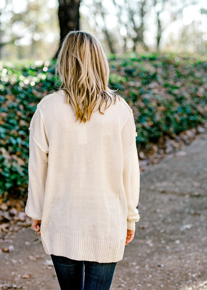 Back view of Blonde model wearing an off white sweater with exposed hem.
