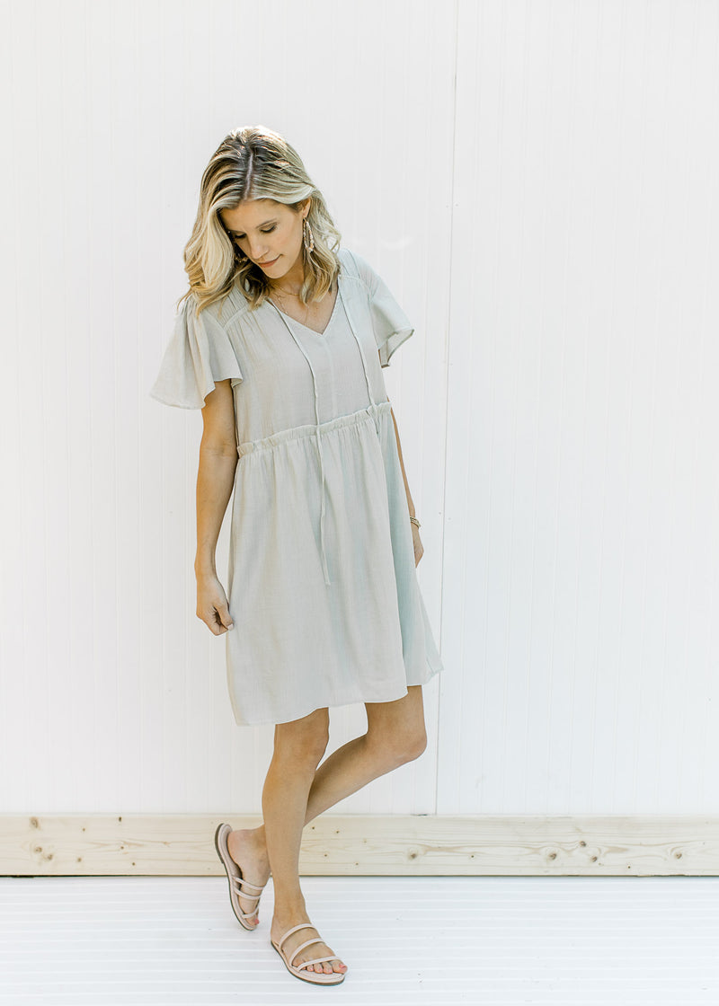 Model wearing a pale mint colored babydoll dress with flutter short sleeves and a v-neck with a tie.