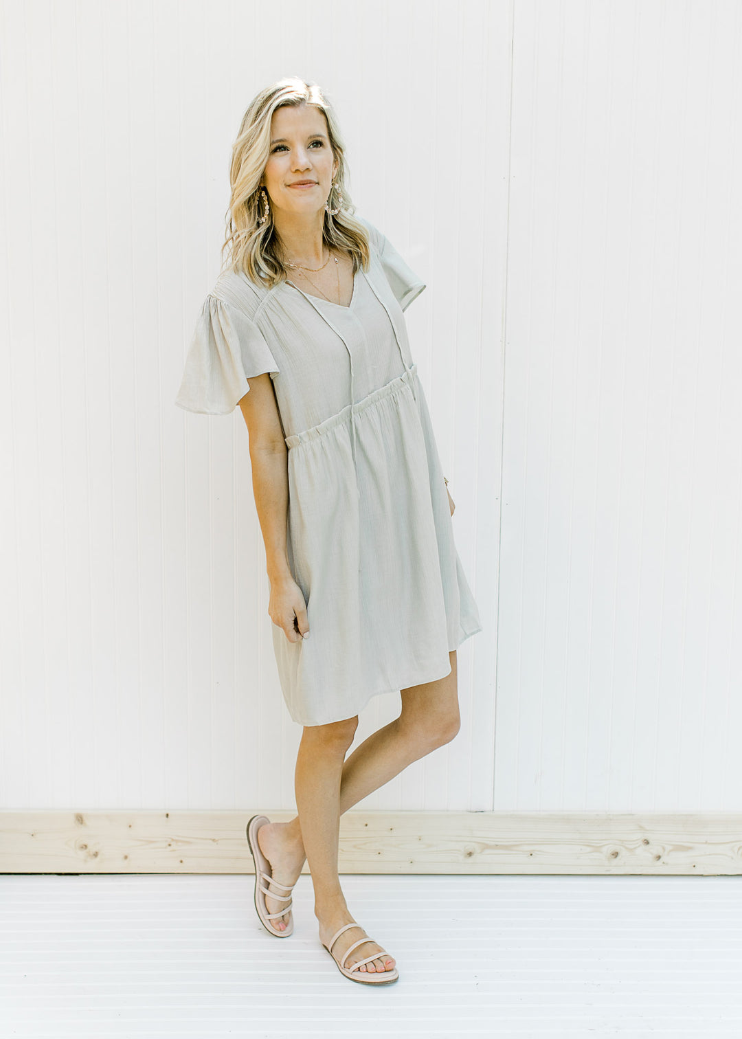 Model wearing a mint colored babydoll dress with flutter short sleeves and a ruffle at the waist. 