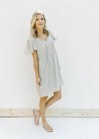 Model wearing a mint colored babydoll dress with flutter short sleeves and a ruffle at the waist. 
