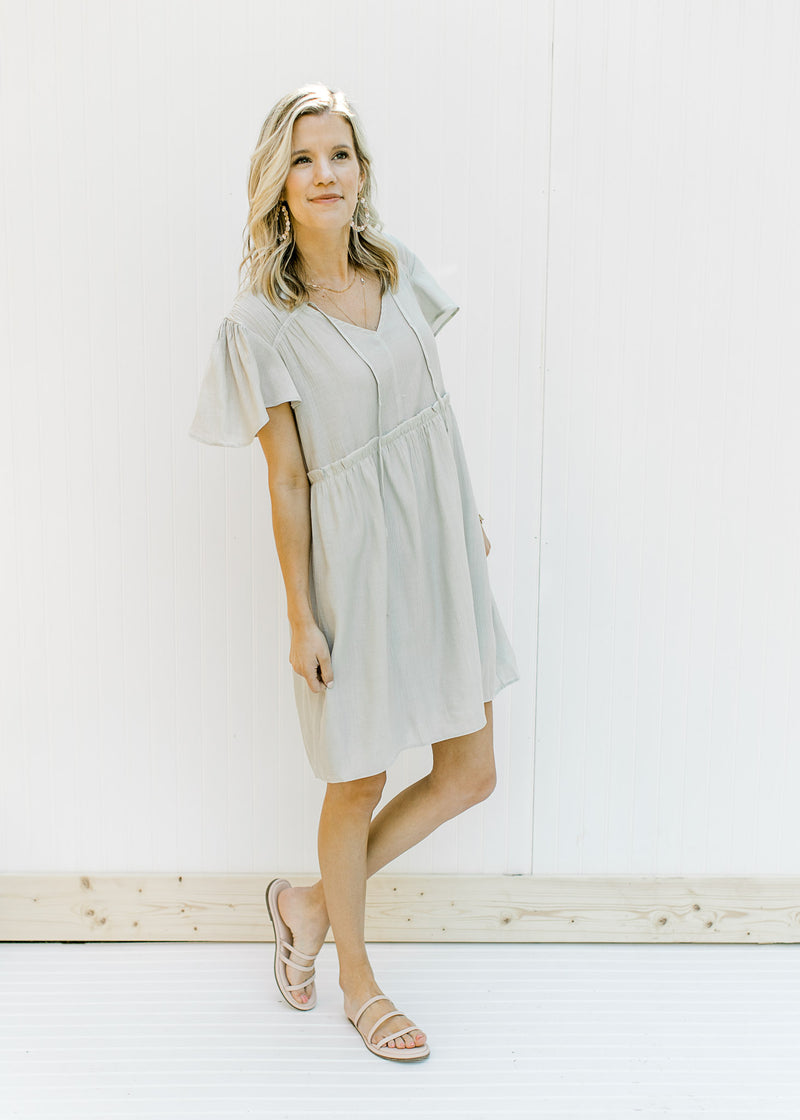 Model wearing a mint colored babydoll dress with flutter short sleeves and a ruffle at the waist. 