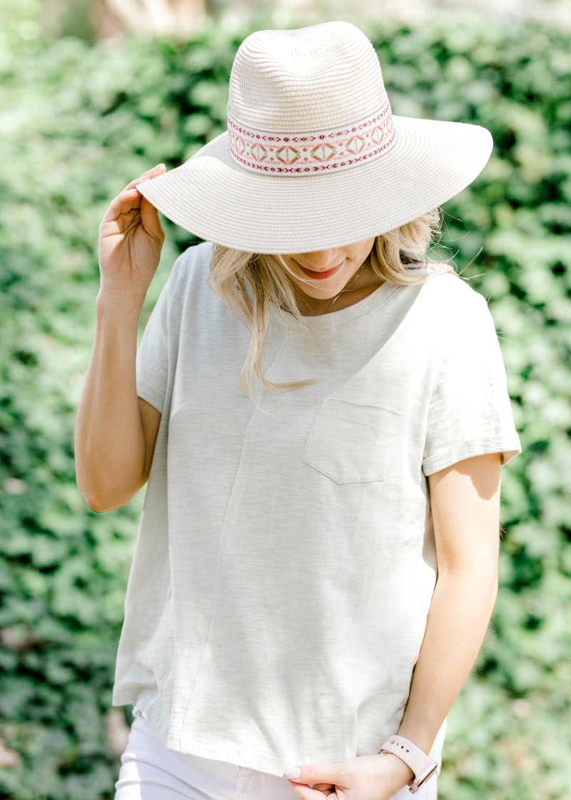Straw hat with aztec band in cream, red, and green on blonde model.