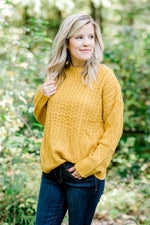 Blonde model wearing mustard cable knit sweater. 