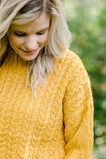 Detail view of Blonde model wearing mustard cable knit sweater.