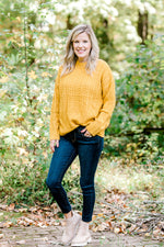 Blonde model wearing mustard cable knit sweater with jeans and booties.