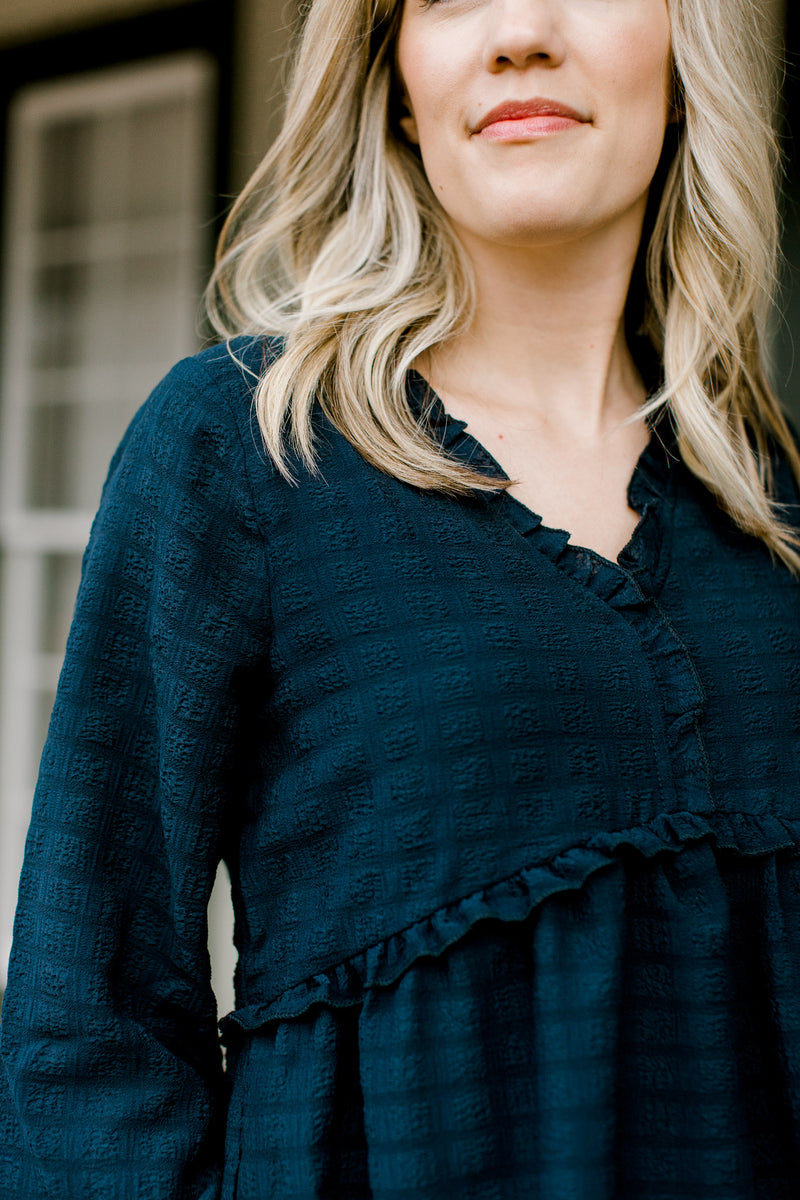 Close up of Blonde model wearing a textured, navy babydoll top.
