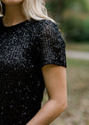 Detail of Blonde model wearing short sleeve black sequin jacket.