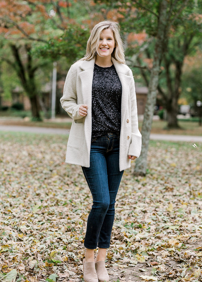 Blonde model wearing short sleeve black sequin jacket and jeans.
