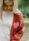 Close up view of Blonde model wearing rust cardigan with pink hearts.