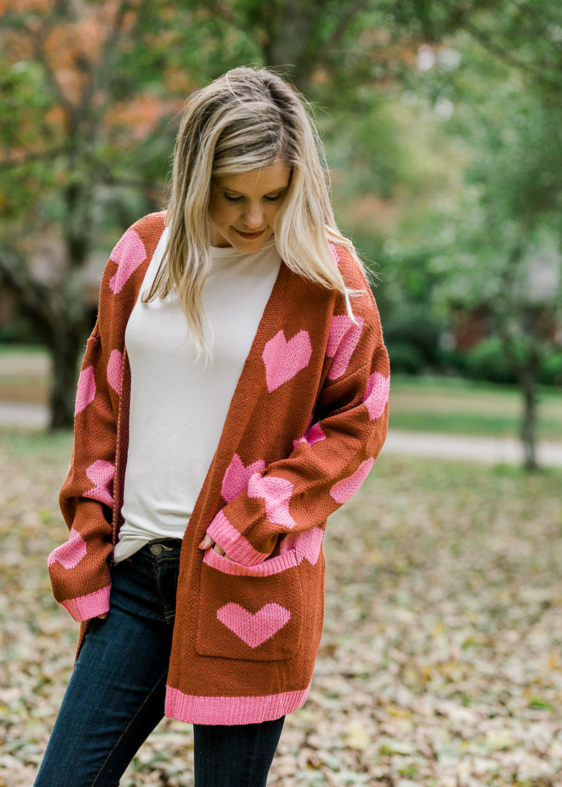 Blonde model wearing rust cardigan with pink hearts.