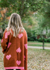 Back view of Blonde model wearing rust cardigan with pink hearts.