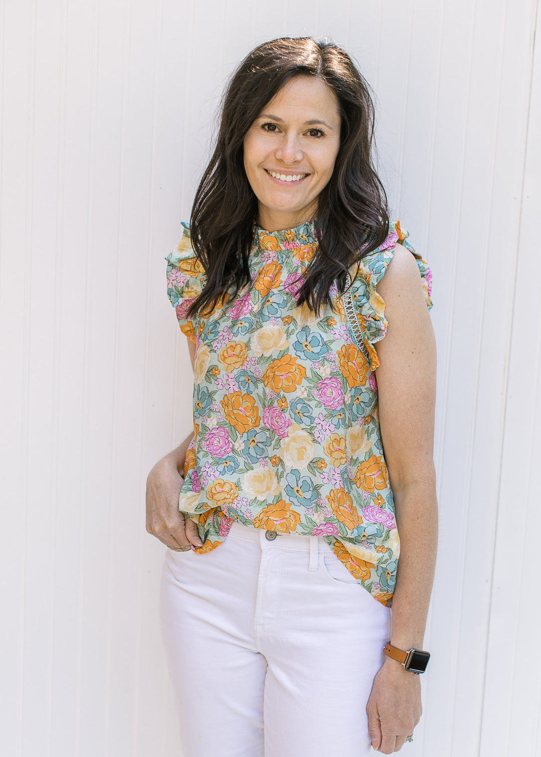 Model wearing a top with a blue background and bright floral pattern with a ruffle at neck and arm. 