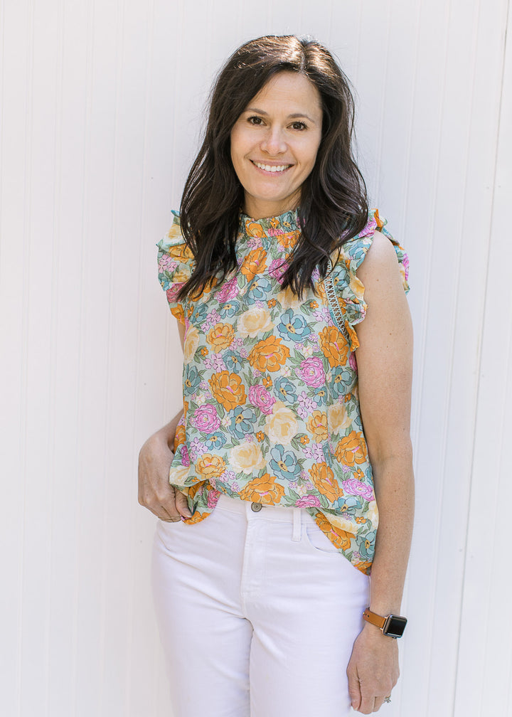 Model wearing a top with a blue background and bright floral pattern with a ruffle at neck and arm. 