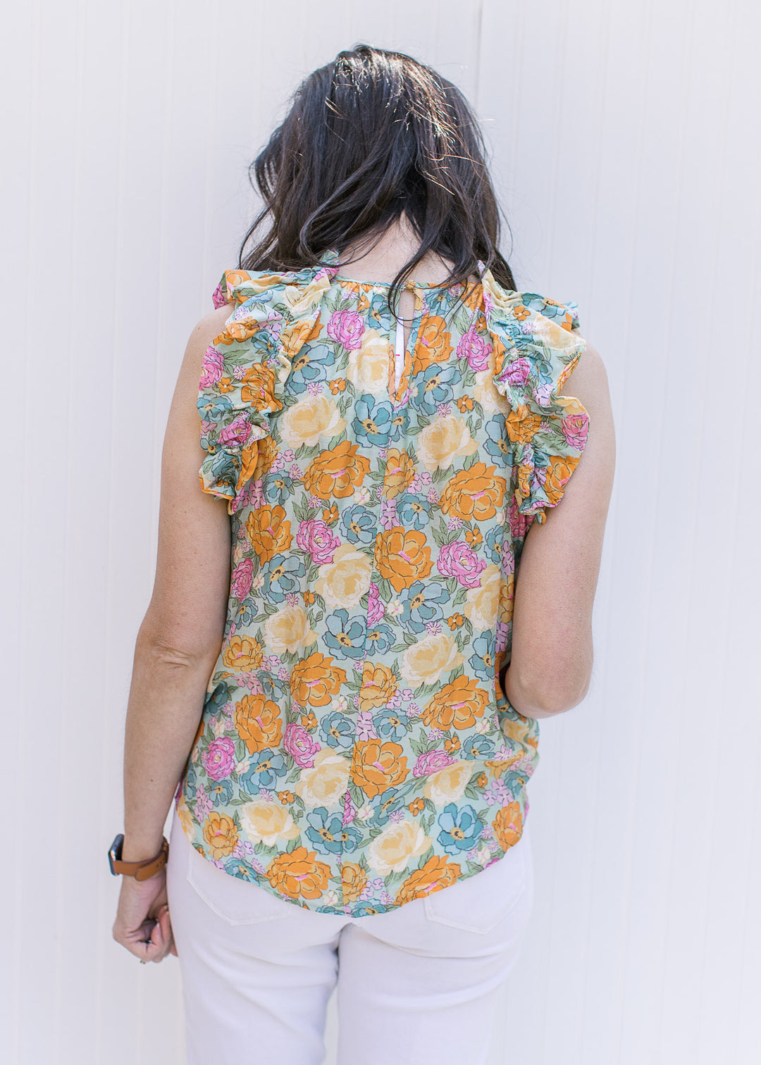 Back view of model wearing a bright floral top with a ruffle on the mock neckline and at arm. 