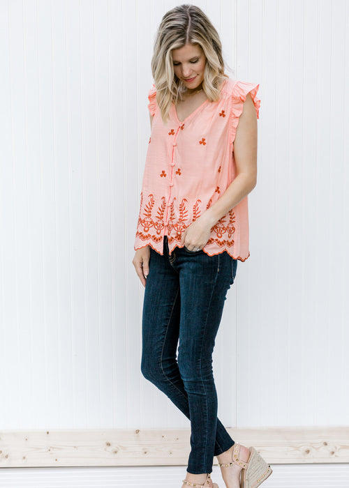 Blonde model wearing peach top with rust embroidery.