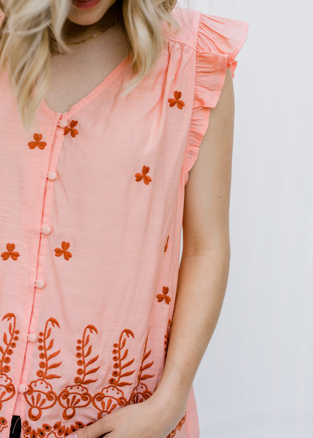 Close up of Blonde model wearing peach top with rust embroidery.