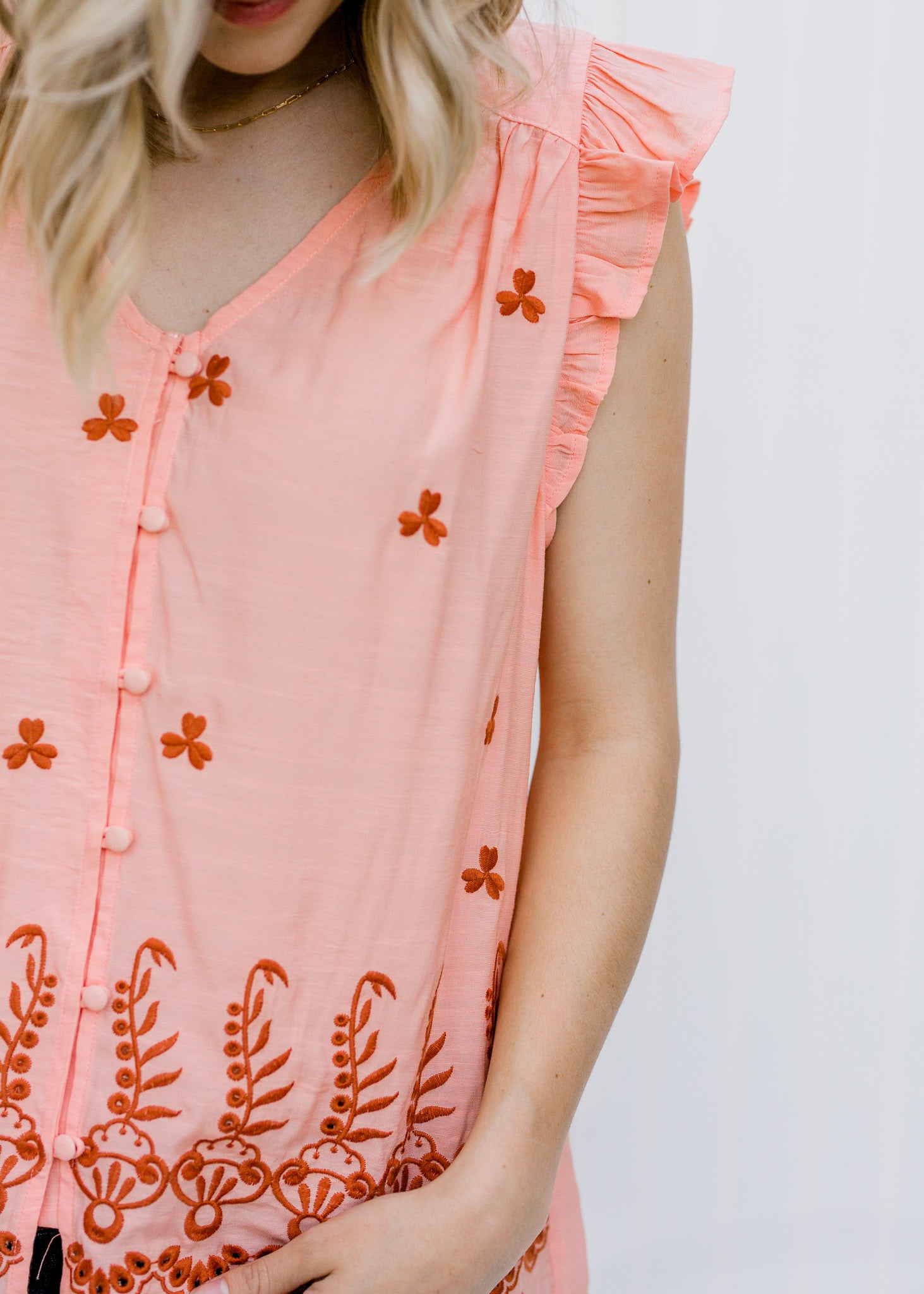 Close up of Blonde model wearing peach top with rust embroidery.