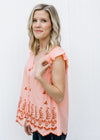 Blonde model wearing peach top with rust embroidery side view.