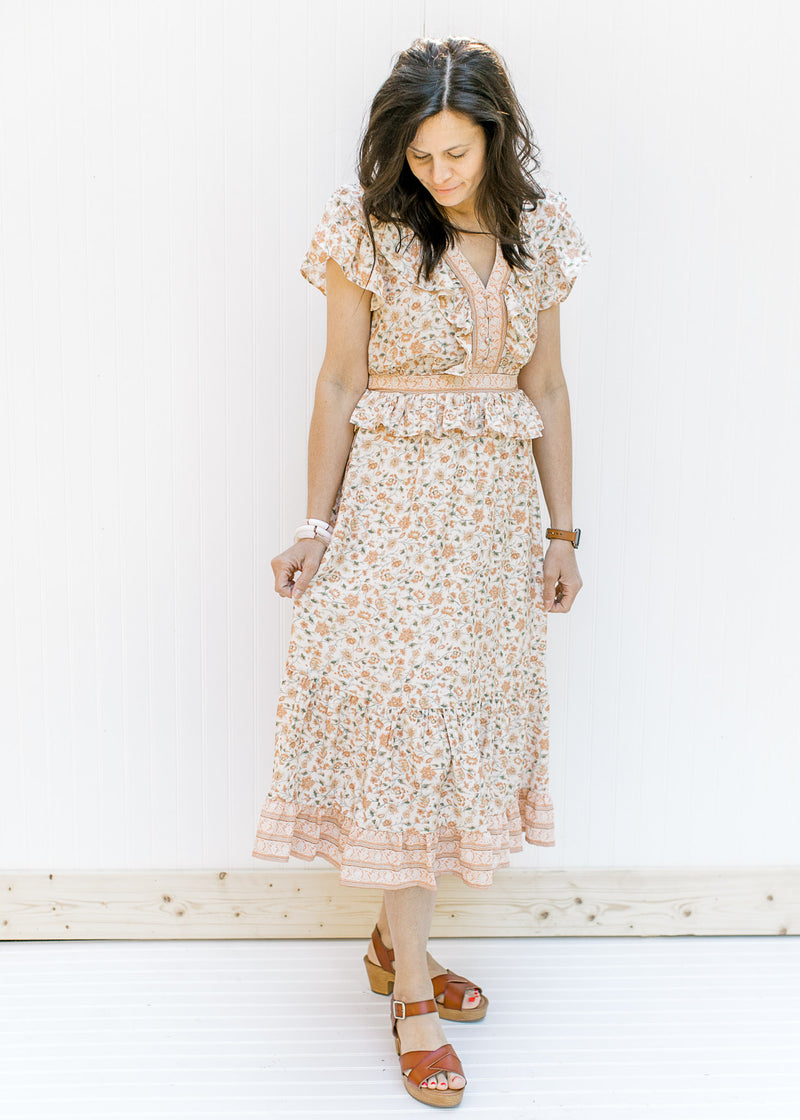 Model wearing a cream midi dress with a peach floral design with a ruffle and elastic at waist. 