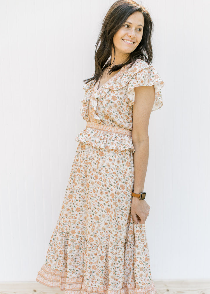 Model wearing a cream short sleeve dress with a peach floral design with a ruffle at waist. 