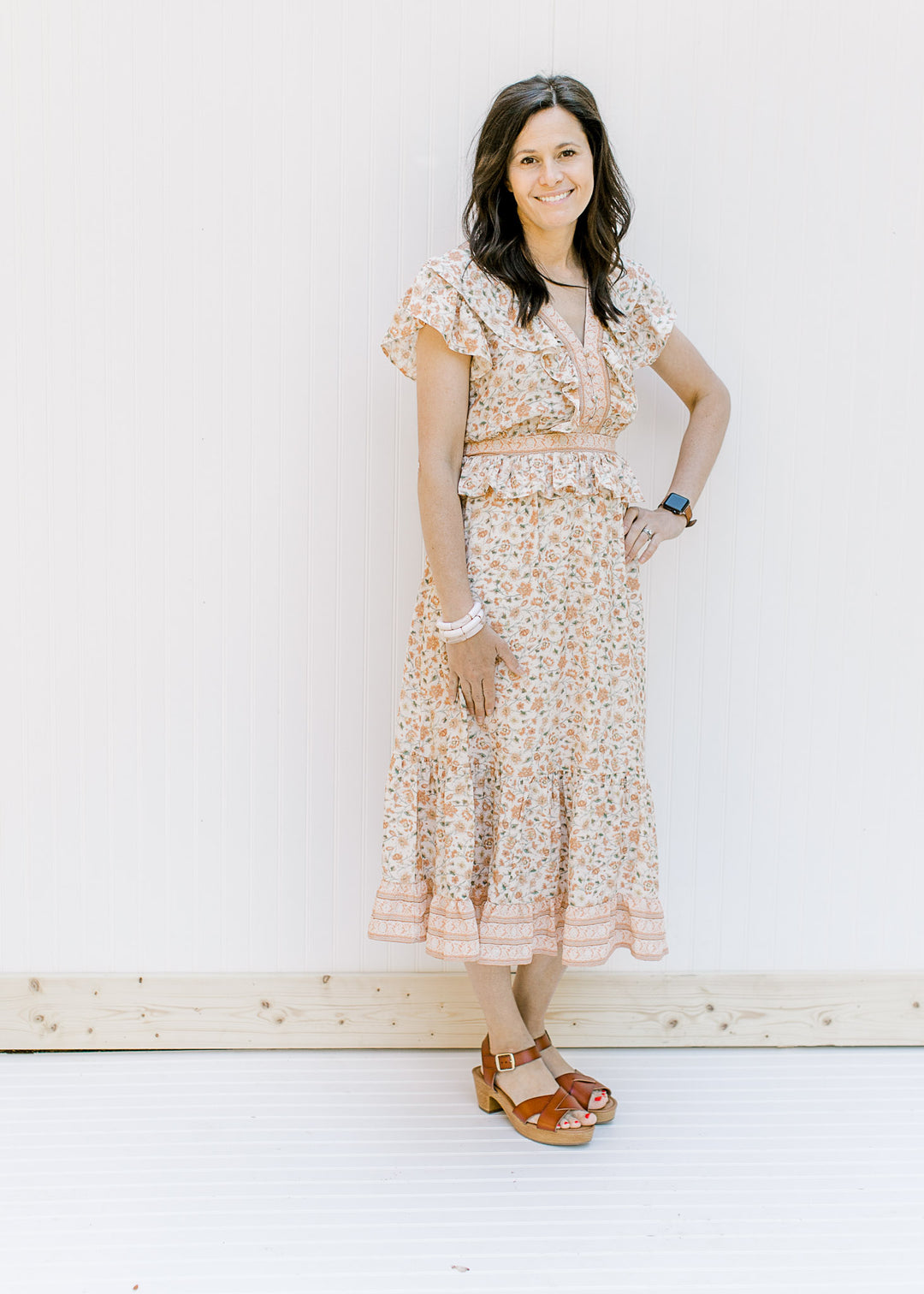 Model wearing a cream v-neck, short sleeve, midi dress with a peach floral design with sandals. 