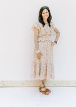 Model wearing a cream v-neck, short sleeve, midi dress with a peach floral design with sandals. 