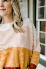Close up view of Blonde model wearing a color block sweater. 