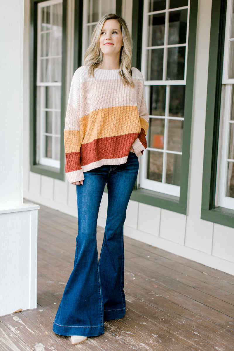 Blonde model wearing a color block sweater with flare jeans. 
