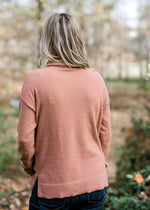 Back view of Blonde model wearing a rose colored sweater with a cowl neck. 