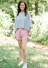 Brunette model wearing pink workout short, loose top and sneakers.