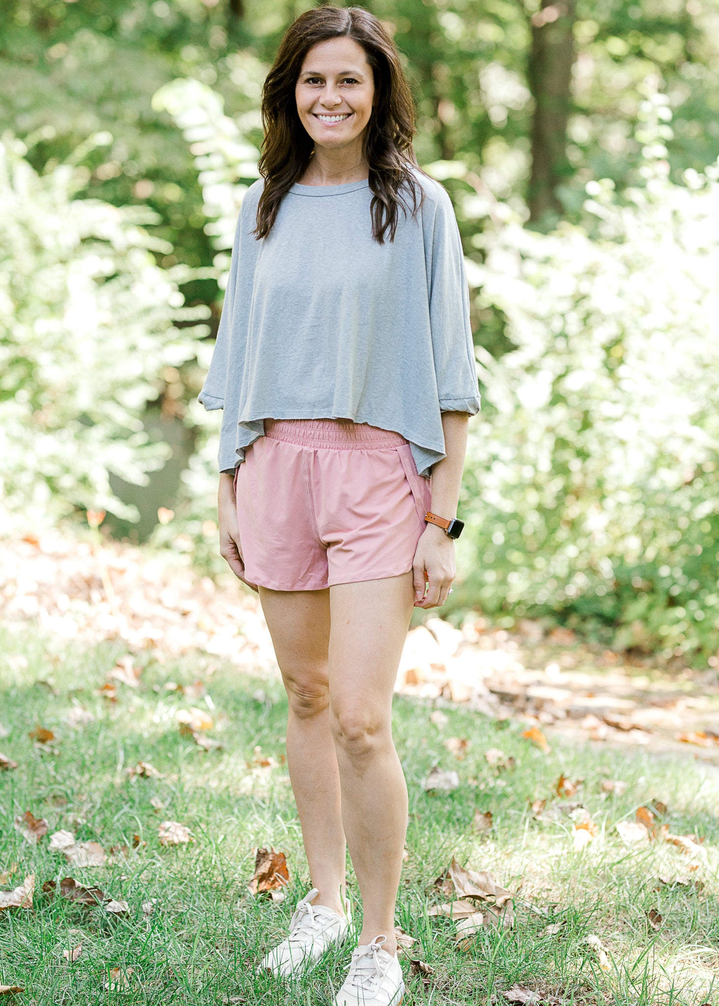 Brunette model wearing pink workout short, loose top and sneakers.