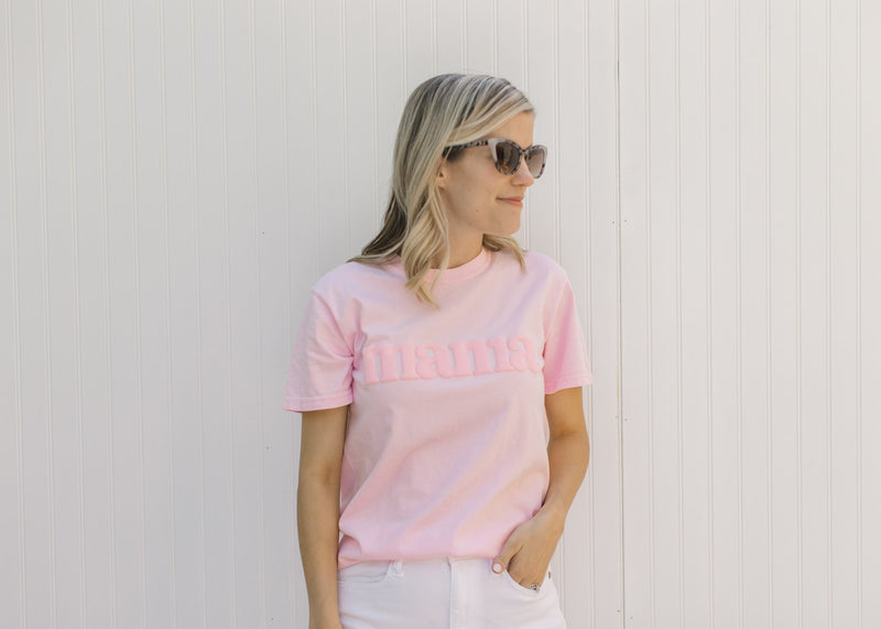 Model wearing sunglasses and a pink short sleeve tee shirt with a raised mama graphic. 