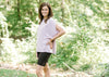 Brunette model wearing pink workout shirt and bike shorts in wooded setting.