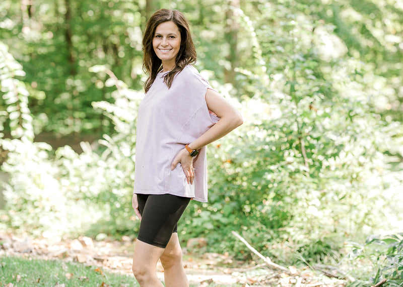 Brunette model wearing pink workout shirt and bike shorts in wooded setting.
