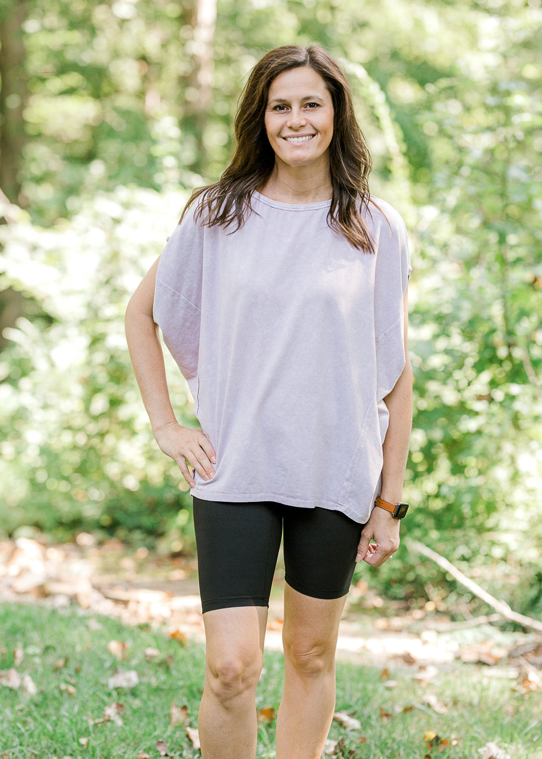Brunette model wearing pink workout shirt and bike shorts and sneakers.