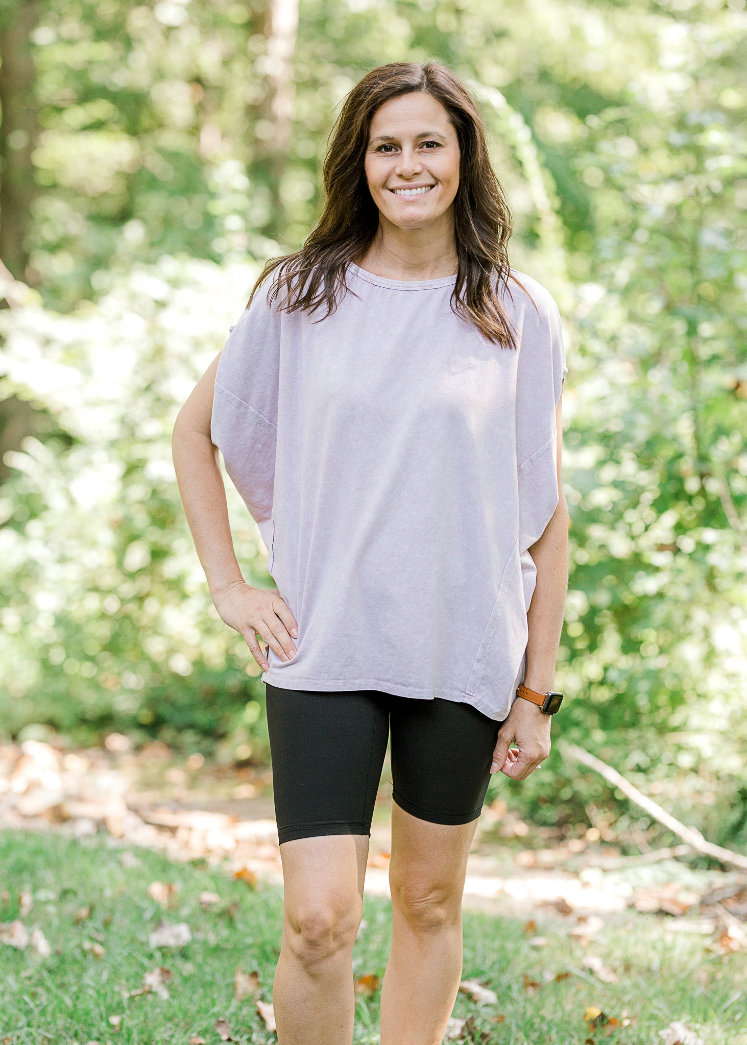 Brunette model wearing pink workout shirt and bike shorts and sneakers.