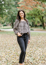 Brunette model wearing cream and black plaid top with jeans.