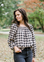 Brunette model wearing cream and black plaid top. 