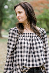Brunette model wearing cream and black plaid top with a square neckline. 