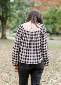 Back view of Brunette model wearing cream and black plaid top.