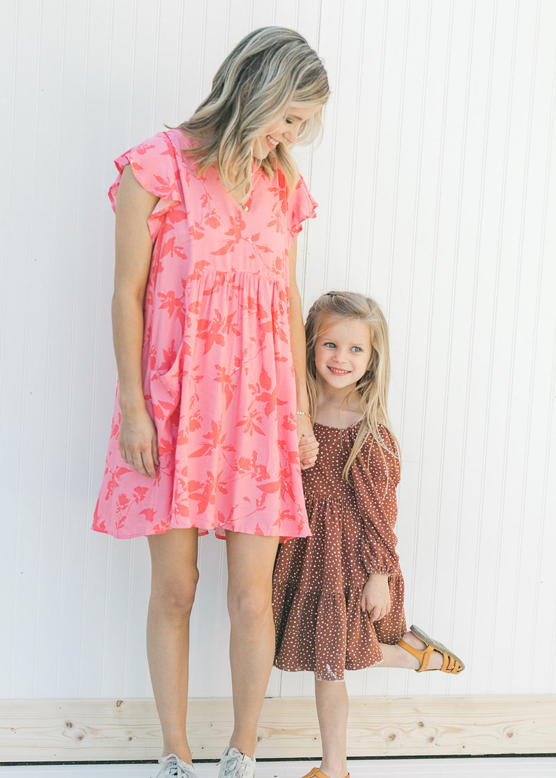 Model wearing a pink dress with a dark pink floral pattern and a babydoll fit with a little girl. 