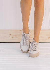Front view of model wearing bone colored sneakers with a star on the side and silver strings.