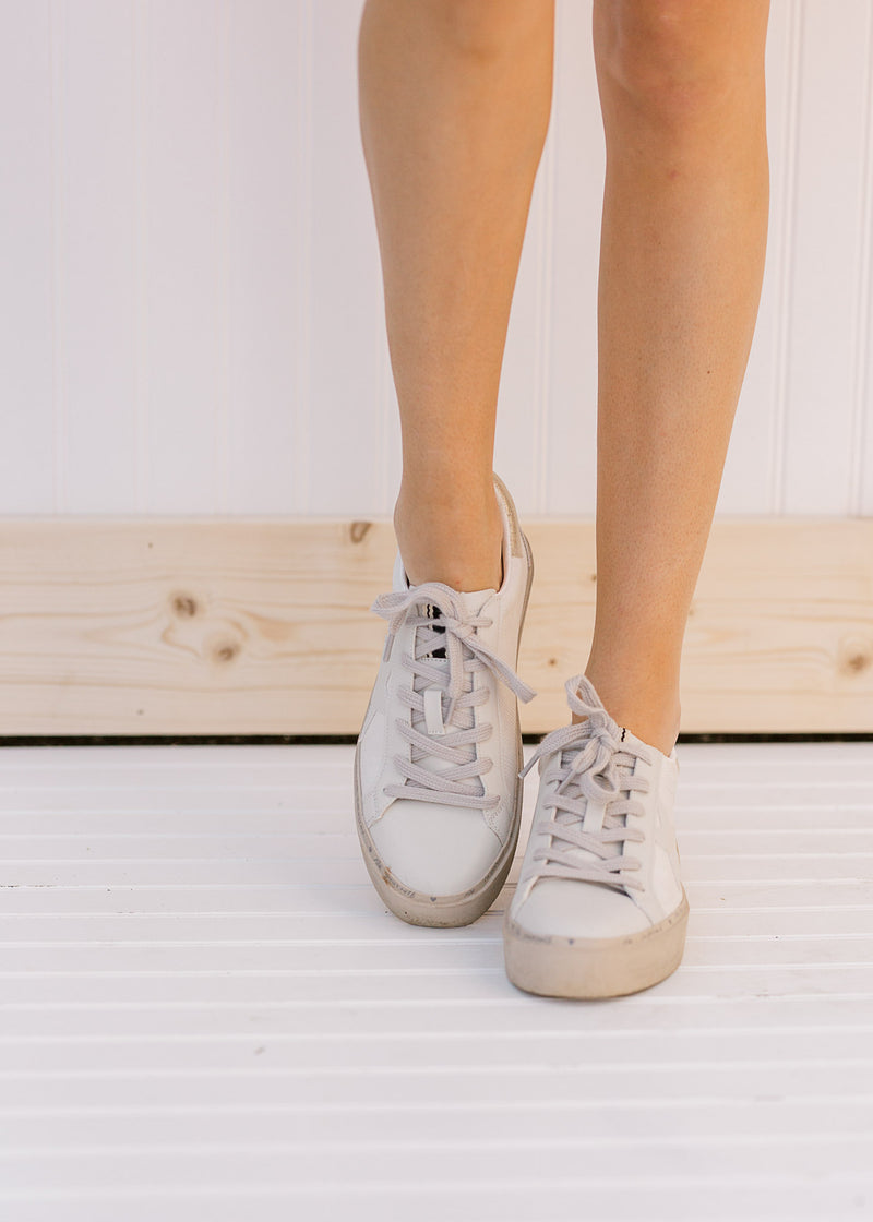 Front view of model wearing bone colored sneakers with a star on the side and silver strings.