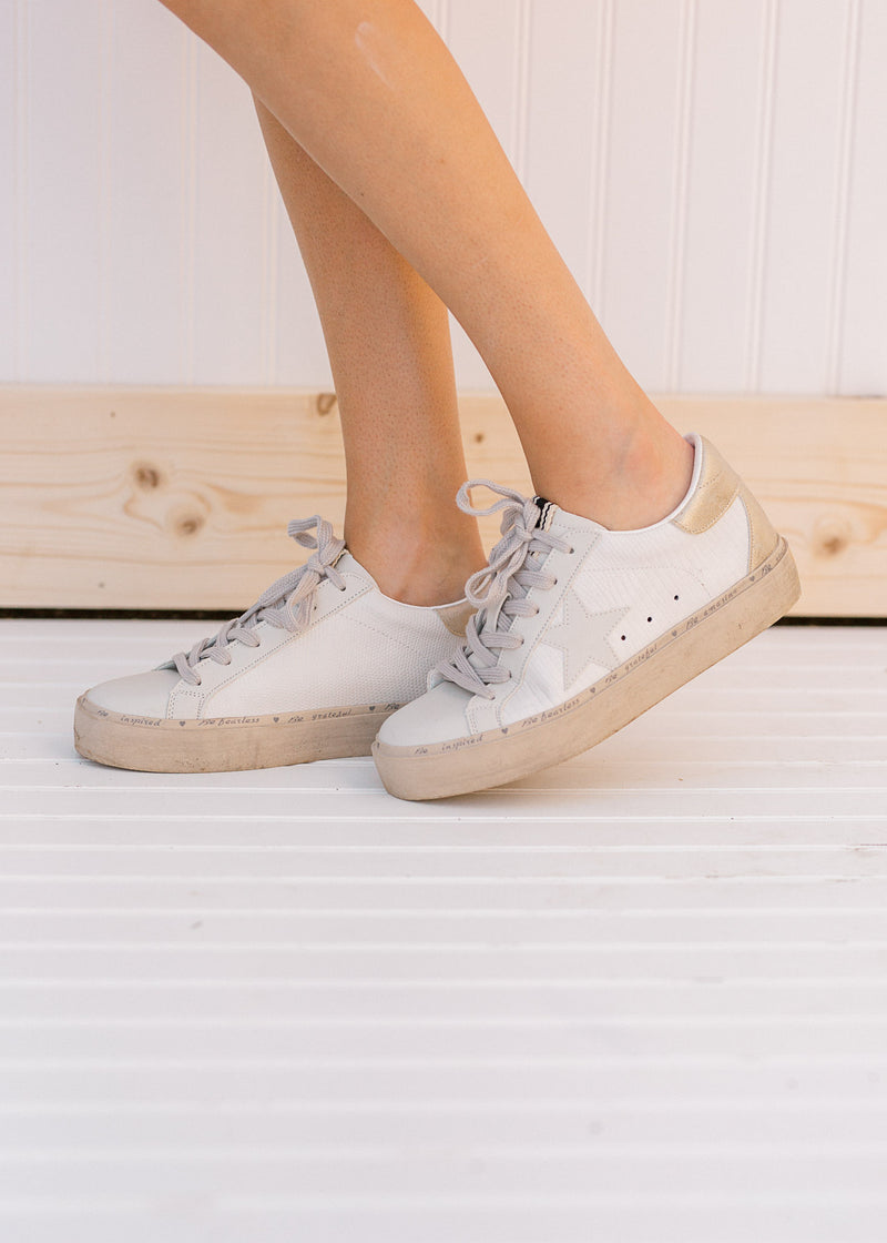 Model wearing bone colored sneakers with a star on the side and a round toe. 