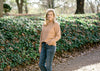 Blonde model wearing a camel color turtleneck sweater with jeans.